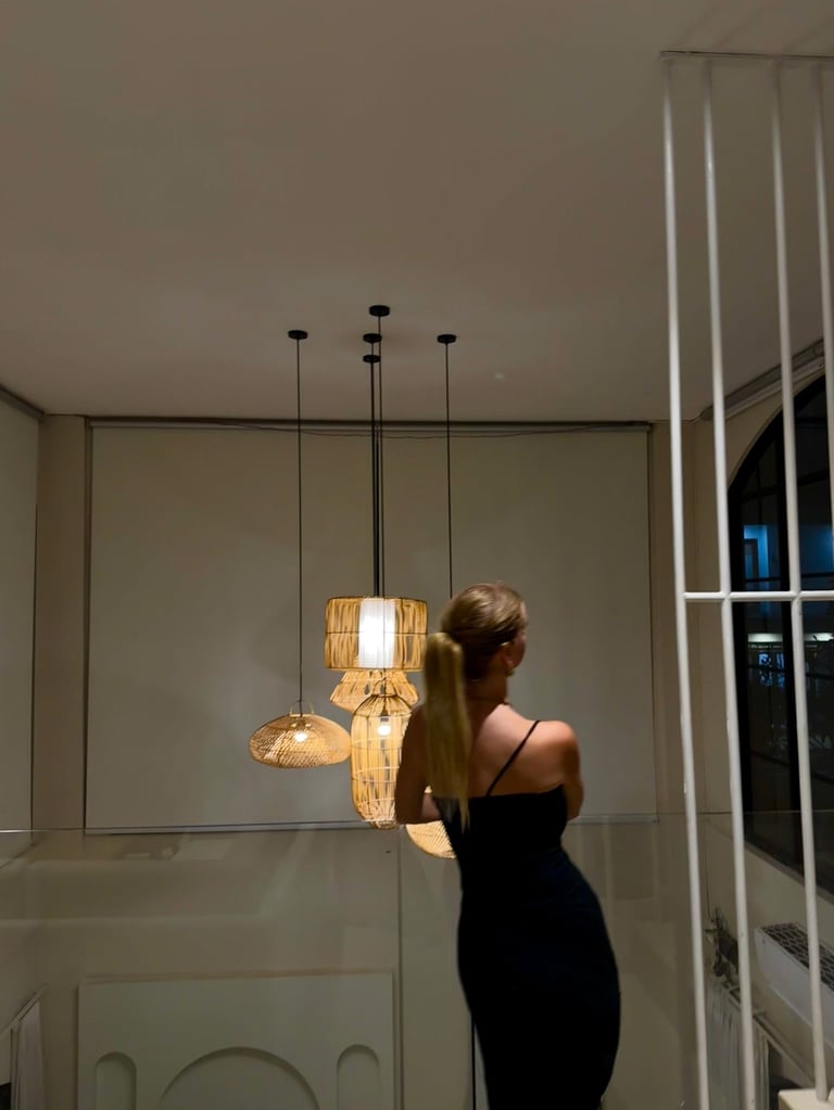 Vrouw in een zwarte jurk staand onder hangende lampen met natuurlijke houten kappen in een modern interieur