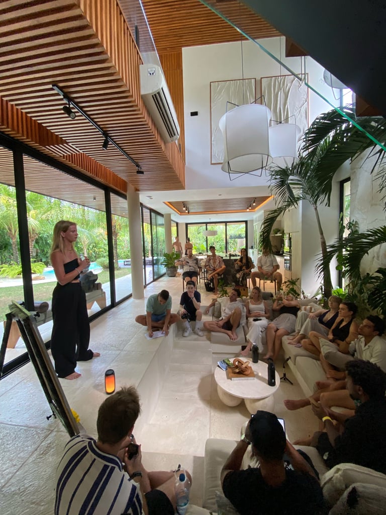 Groep mensen bij een presentatie of les in een moderne, lichte ruimte met houten plafond, planten en grote ramen