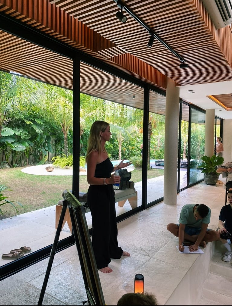 Woman in black dress standing by large glass doors in modern home with wooden slatted ceiling, overlooking garden